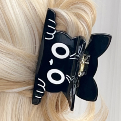 Black cat hair clip with white eyes on blonde hair against a white background