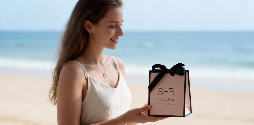 Woman holding a black gift bag with 'SHB Studio' on a beach