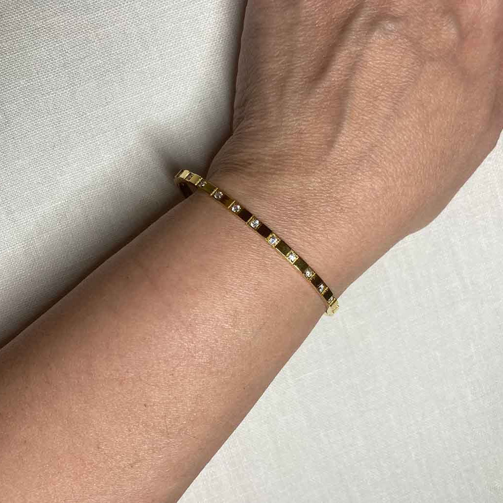 Gold bracelet on a wrist against a neutral background