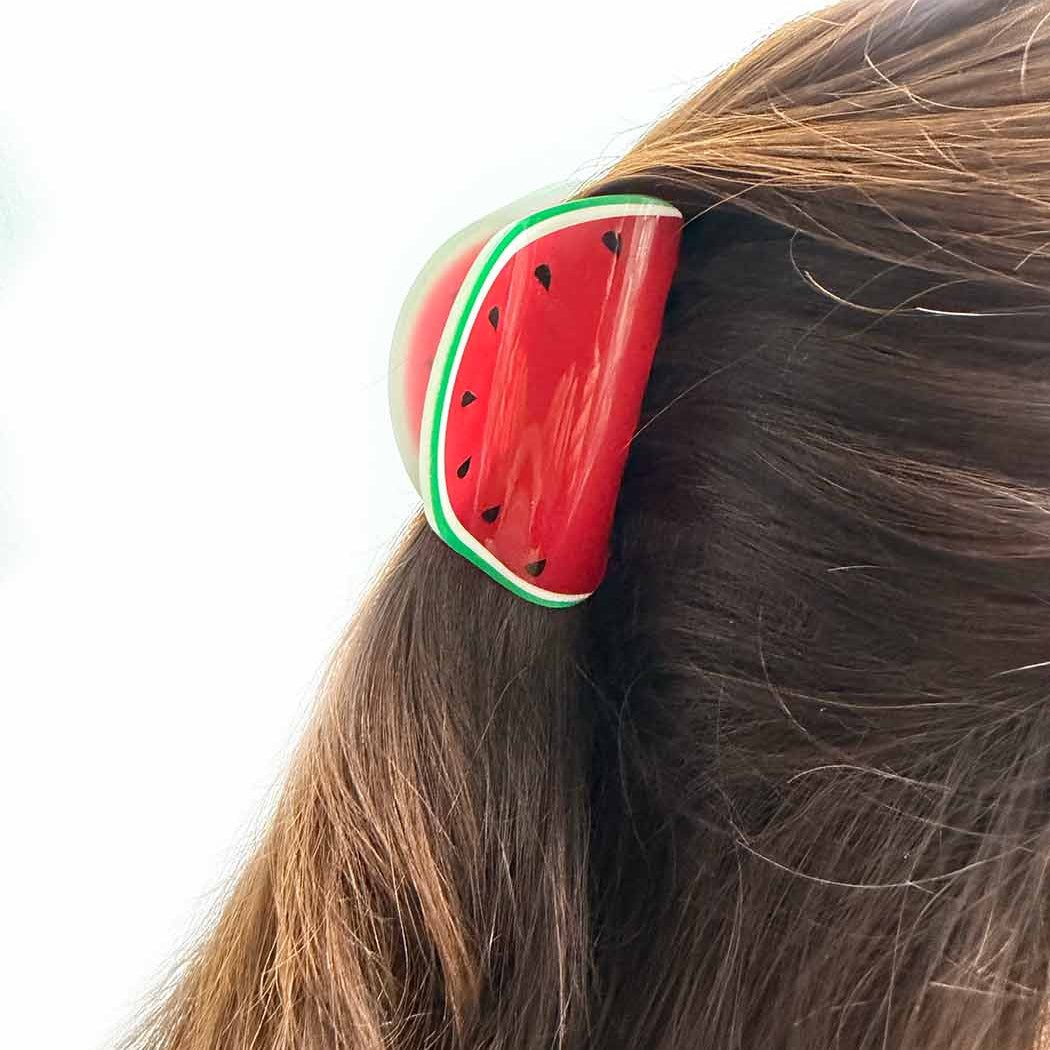 Watermelon-themed hair clip on a person's hair against a white background